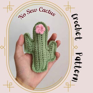 May include: A crocheted cactus in light green with a pink flower, held in a hand. The image includes the text "No Sew Cactus" and "Crochet Pattern" in a decorative frame.