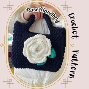 May include: A black crocheted handbag with a white crocheted rose and green leaves. The handbag has a simple design and is perfect for everyday use. "Rose Handbag Crochet Pattern" is written on the image.