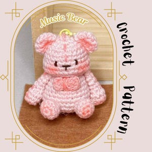 Può includere: Un orso di peluche rosa lavorato a uncinetto con un fiocco. L'orso è seduto su una superficie marrone. Il testo "Music Bear Crochet Pattern" è scritto sul lato destro dell'immagine.