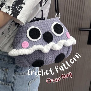 May include: A gray crocheted bag shaped like a creature with large white and black eyes, a black nose, pink cheeks, and a white wavy trim. The bag features a black strap and has the text Crochet Pattern Crow Bag printed on the lower right side.
