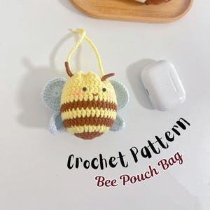 Könnte beinhalten: Eine gehäkelte Bienen-Tasche mit gelb-braun gestreiftem Körper, hellblauen Flügeln und einem gelben Kordelzug. Der Text "Crochet Pattern Bee Pouch Bag" ist in Schwarz und Rot geschrieben.