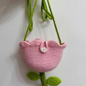 May include: A pink crocheted tulip-shaped bag with a green crocheted stem and leaves. The bag has a small white button on the front.