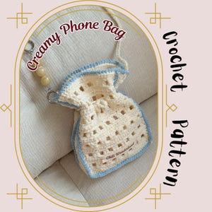 Puede incluir: Bolso de teléfono de ganchillo color crema con ribete y correa azul claro. El bolso tiene un cierre de cordón y un dije de cuentas. El texto "Creamy Phone Bag" y "Crochet Pattern" son visibles.