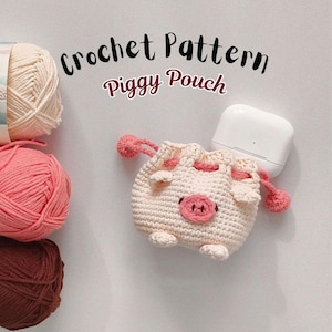 May include: A crocheted piggy pouch in cream with pink accents, holding a white electronic device. The pouch features a pink snout, ears, and drawstring closure. The words "Crochet Pattern Piggy Pouch" are written above the pouch.