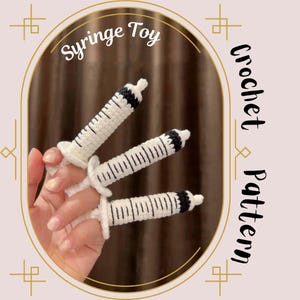 May include: Three white and black crocheted syringe toys with a black and white striped pattern. The toys are on a person's fingers. The image has the text "Syringe Toy Crochet Pattern".