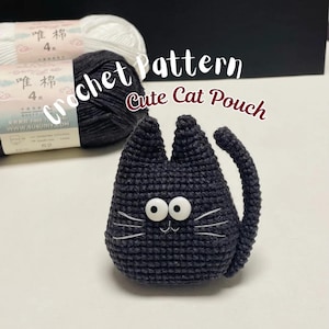 May include: A dark gray crocheted cat pouch with large white button eyes, embroidered white whiskers, and a curved tail. The text "Crochet Pattern Cute Cat Pouch" is visible above the cat, with two skeins of yarn in the background.