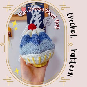 Puede incluir: Un bolso de ganchillo con forma de copa de helado, con colores azul, blanco y amarillo, coronado con una cereza roja. El texto "Ice Cream Bowl Bag" y "Crochet Pattern" es visible en la imagen.