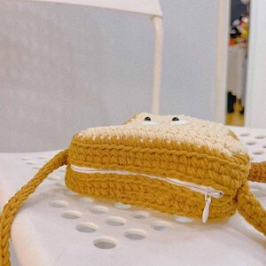 K&ouml;nnte beinhalten: Eine geh&auml;kelte braune und wei&szlig;e Tasche in Brotform mit Rei&szlig;verschluss und Trageriemen.