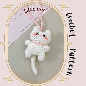 Puede incluir: Un gato blanco de ganchillo con mejillas rosas y ojos negros, que lleva una bufanda rosa. El gato está suspendido por una cuerda rosa. La imagen incluye el texto "Little Cat" y "Crochet Pattern".