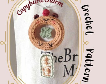 May include: A crocheted capybara charm with a clover charm hanging from it. The charm is brown with a red nose and white eyes. The text "Capybara charm" is written on the top of the image. The text "Crochet Pattern" is written on the right side of the image.