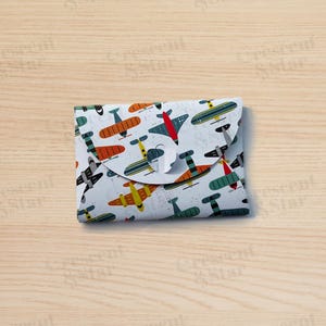 Op de afbeelding: Een witte envelop met een kleurrijk patroon van vliegtuigen. De envelop heeft een flap die overklapt om hem te sluiten.