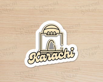 May include: A white sticker with a yellow outline features a simple line drawing of a building with a dome on top. The text "Karachi" is written in a yellow, stylized font below the building.