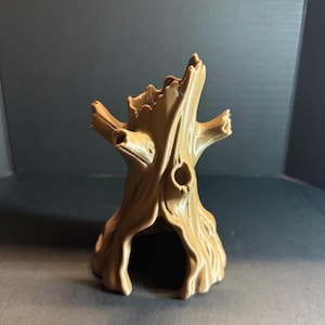 May include: A light brown, three-dimensional printed tree stump sculpture featuring a hollow centre, textured bark details, and several protruding branch stubs. The object has a wide, arched opening at the base and a jagged, open top structure.