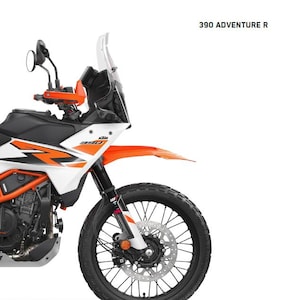 以下が含まれることがあります： 白、オレンジ、黒の390 Adventure Rオートバイ。フロントホイールは黒で、シルバーのディスクブレーキが付いています。オートバイには、フロントガラス、サイドミラー、およびテキスト「REPAIR MANUAL 2025」と「390 ADVENTURE R」があります。