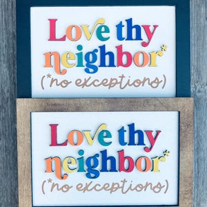 May include: Two framed signs with the message "Love thy neighbor (*no exceptions)". The text is in colorful, raised letters on a white background. One frame is dark blue, the other is brown.