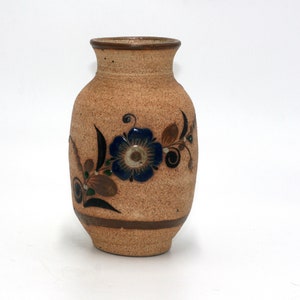 May include: A small, brown ceramic vase with a floral design. The vase has a blue flower with brown and green leaves.