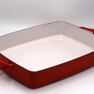 May include: Red enamel cast iron baking dish with two handles. The dish is empty and has a white interior.