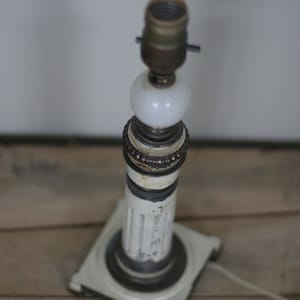 May include: A vintage table lamp with a white and brass finish. The lamp features a square base, a fluted column, and a white globe. The lamp's measurements are approximately 12 inches tall.