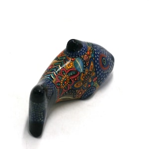 May include: A hand-painted ceramic fish figurine with blue, green, yellow, orange, and red floral patterns. The fish has a black eye and is lying on its side.