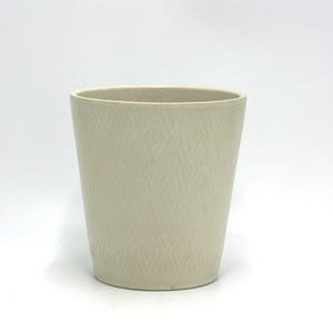 May include: A white ceramic planter with a diamond pattern. The planter is a cylindrical shape with a slightly flared top.