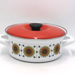 May include: A vintage white enamel pot with a red lid and black handle. The pot features a floral pattern in shades of green, orange, and brown. It has two white handles on either side, perfect for cooking.