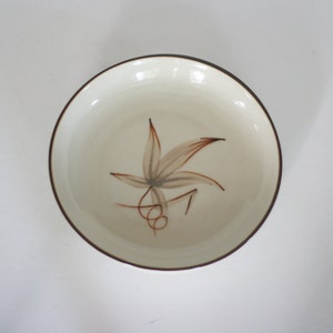 May include: A white ceramic bowl with a brown rim and a stylized brown leaf design.