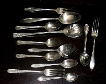 May include: A set of silverware, including forks, spoons, and serving spoons, all made of polished silver. The silverware is arranged on a dark surface.