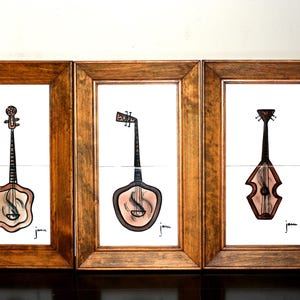 May include: Three framed illustrations of different musical instruments. Each illustration is in black and white with a brown and pink wash. The instruments are a banjo, a guitar, and a violin. Each frame is made of dark wood.