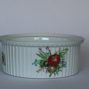 May include: White ceramic baking dish with a fluted rim and a floral design featuring a tomato, onion, and other vegetables.