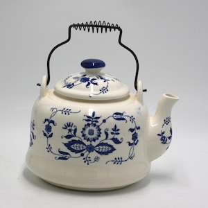 May include: Cream-colored ceramic teapot with blue floral patterns and a black metal handle. The lid has a blue knob and matching floral design. The spout is on the right side. A classic design for tea lovers.