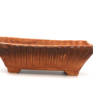 May include: A rectangular brown ceramic planter with a textured surface and four small feet.