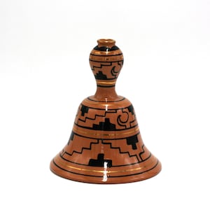 May include: A small, brown ceramic bell with black and gold geometric designs. The bell has a wide base and a narrow neck.