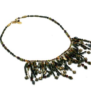 May include: A gold and green beaded necklace with a fringe of beads hanging from the bottom. The necklace is made of various sizes and shapes of beads, including round, oval, and rectangular beads.