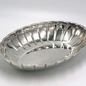 May include: A silver-colored, oval-shaped serving dish with a scalloped rim. The dish has a fluted design on the sides, creating a textured appearance. The interior is smooth and reflective, suitable for serving food or as a decorative piece.
