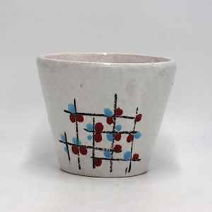 May include: A white ceramic planter with a textured surface. The planter features a grid design with red and blue floral accents. The interior of the planter is a light beige color.