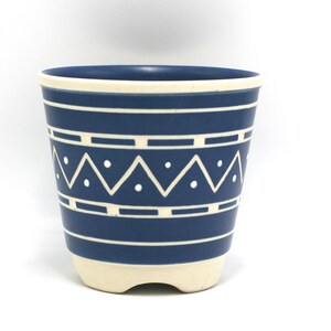 May include: A blue ceramic planter with a white geometric pattern. The planter has a white rim and a white base with three feet.