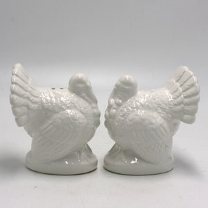 May include: A set of two white ceramic turkey salt and pepper shakers. The turkeys are facing each other and have detailed features.