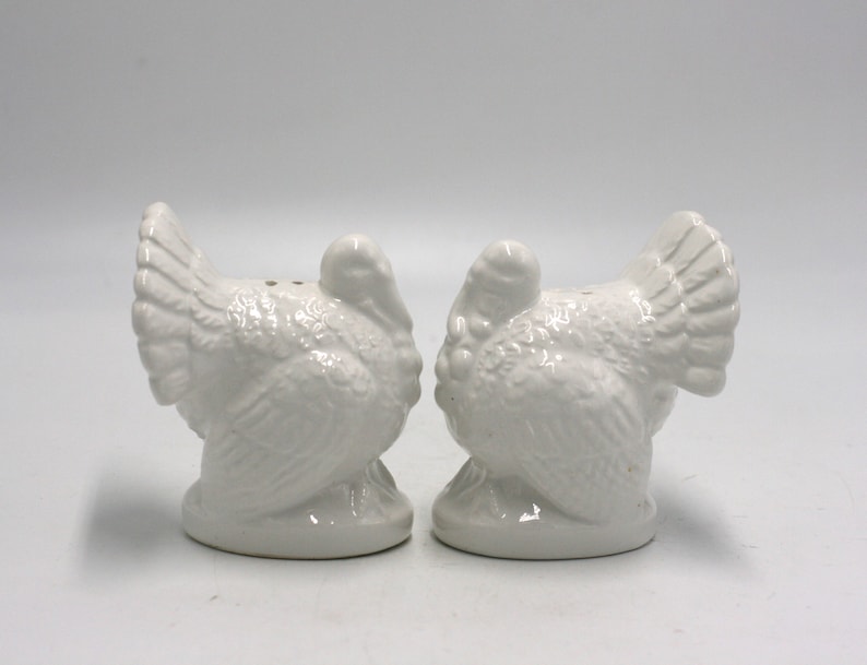 May include: A set of two white ceramic turkey salt and pepper shakers. The turkeys are facing each other and have detailed features.