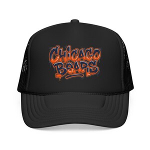 May include: A black trucker hat featuring a mesh back and a solid front panel. The front displays the text CHICAGO BEARS in a stylized, graffiti-inspired font with orange and dark blue lettering, featuring a dripping paint effect on the letters.