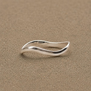 Puede incluir: Un anillo de plata pulida que presenta un diseño ondulado continuo y suave. La banda tiene una superficie metálica reflectante con un grosor constante a lo largo de su forma curva y fluida, creando una forma circular simple y elegante.