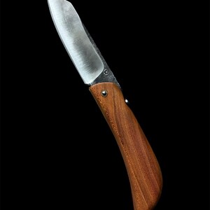 Könnte beinhalten: Ein Klappmesser mit polierter Stahlklinge und einem gebogenen Holzgriff. Der Griff hat eine warme braune Farbe, und die Klinge ist mit einer kleinen Metallniete befestigt. Das Messer ist vor einem schwarzen Hintergrund platziert.