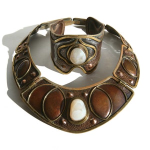 May include: A vintage jewelry set featuring a necklace and matching bracelet. The set has a copper and brass finish with oval and teardrop-shaped brown accents and a central white stone. The bracelet is a cuff style.