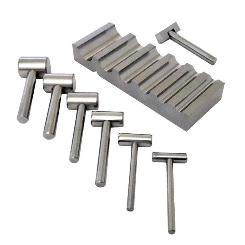 May include: A set of six small, silver-colored metal hammers with cylindrical handles and a stepped metal block. The hammers have a T-shaped design. The block has a series of angled grooves.