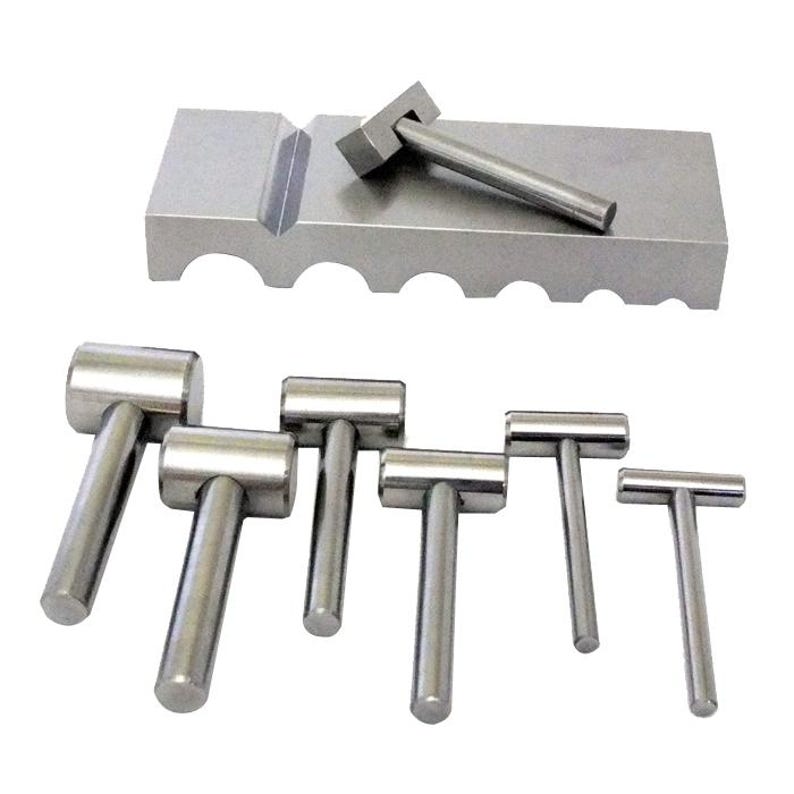 May include: A set of silver metal hammers of varying sizes, with a matching metal block. The hammers have cylindrical heads and handles, and the block has a groove and several cutouts. The tools are arranged on a white background.