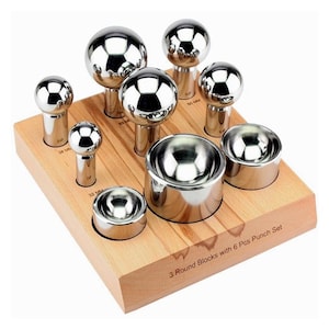 May include: A metal punch set with six spherical punches and three round blocks. The punches and blocks are made of shiny metal and are set on a wooden base. The sizes are marked in mm. The text "3 Round Blocks with 6 Pcs Punch Set" is visible.