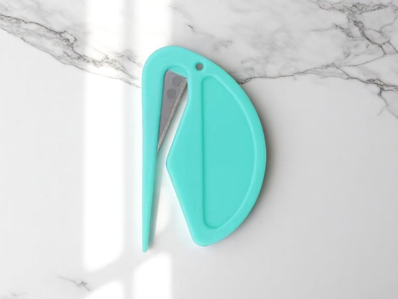 K&ouml;nnte beinhalten: Ein t&uuml;rkisfarbener Brief&ouml;ffner mit einer silbernen Klinge. Der &Ouml;ffner hat einen gebogenen Griff und ein abgerundetes Ende mit einem kleinen Loch in der N&auml;he der Oberseite. Das Design ist modern und minimalistisch.