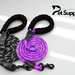 May include: Two dog leashes, one black and white, the other purple, are coiled on a white surface. Each leash has a black padded handle and a black metal clasp. The leashes are from Pawsome Stuff Pet Supplies.