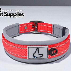 Puede incluir: Collar para perros rojo y gris con una tira reflectante y una hebilla negra. El collar tiene un interior acolchado gris y un parche rectangular con un dibujo de perro. El texto "PAWSOMESTUFF" y "Pet Supplies" es visible.