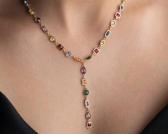 May include: A gold-toned necklace with a Y-shaped pendant. The necklace features a series of colorful, geometric gemstones in various shapes, including squares, rectangles, and ovals. The gemstones are in shades of red, blue, green, purple, and yellow.