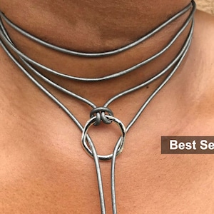Puede incluir: Un collar choker plateado con un colgante de anillo plateado. El collar está hecho de múltiples hebras de cordón y está en capas. El collar es un éxito de ventas.